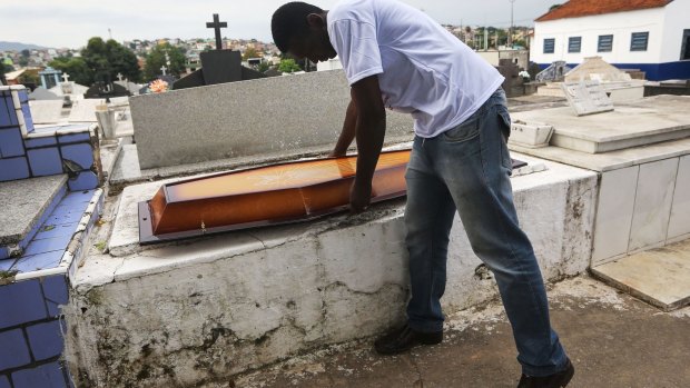 Leonardo Martins da Silva prepares to place the top section over the casket before the burial of his son.