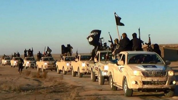 Islamic State militants hold up their weapons and wave the group's flags on their vehicles in a convoy in Raqqa, Syria.