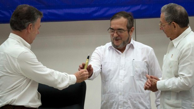 Colombian President Juan Manuel Santos, left, hands the bullet pen to FARC Commander Timochenko, centre, as Cuban President Raul Castro watches.