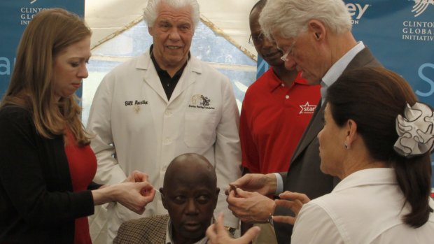 Former US President Bill Clinton and and Chelsea Clinton, left, help a Kenyan to fit hearing aids.