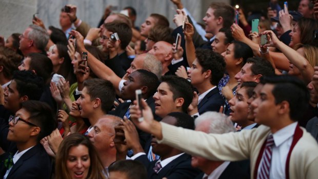 People raise their phones and cameras as Pope Francis passes.