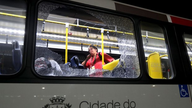 A member of the media stands near a shattered window on a bus in the Deodoro area of Rio de Janeiro after it came under attack.