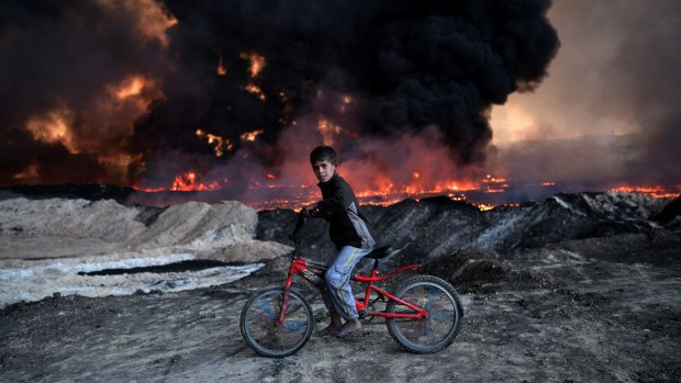 A boy pauses on his bike as he passes an oil field that was set on fire by retreating IS fighters ahead of the Mosul offensive in Qayyarah, Iraq. 