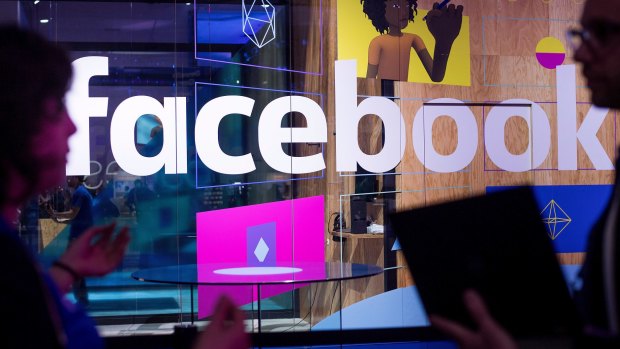 Conference workers speak in front of a Facebook demo booth.