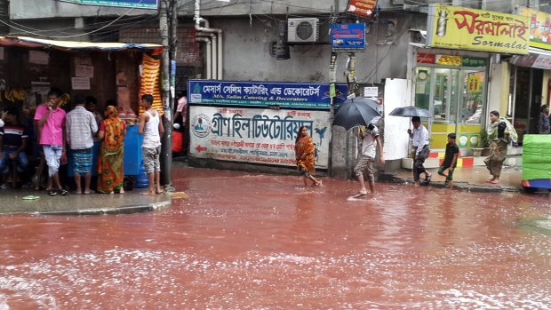 People wade past a road turned red after blood from sacrificial animals mixed with water from heavy rainfall in Dhaka on Tuesday.