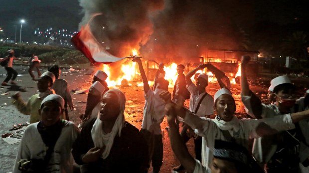 Muslim protesters chant slogans near burning police trucks during the clashes.