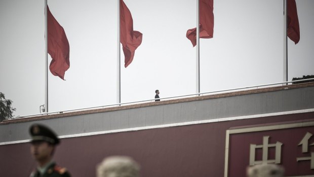 A paramilitary police officer and a security official stand guard near red flags at Tiananmen Gate in Beijing, China.