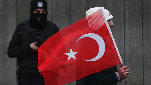 A man with a Turkish flag walks past a police officer during a memorial outside the Reina club. The killer remains at large four days after the attack.