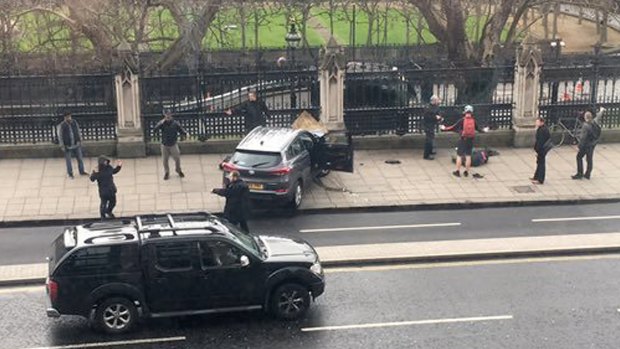 People stand near a crashed car and an injured person lying on the ground, right, on Bridge Street near the Houses of Parliament in London on Wednesday.