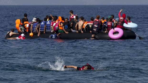 A Syrian man swims in front of a dinghy full of refugees off the Greek island of Lesbos.