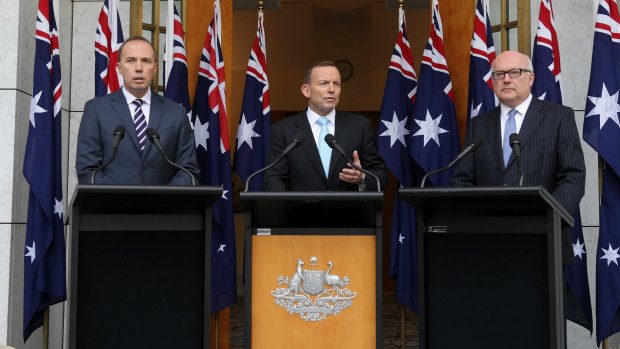 Immigration Minister Peter Dutton, Prime Minister Tony Abbott and Attorney-General Senator George Brandis stand in front of ten flags at a press conference the day after Mallah appeared on <i>Q&A</i>.