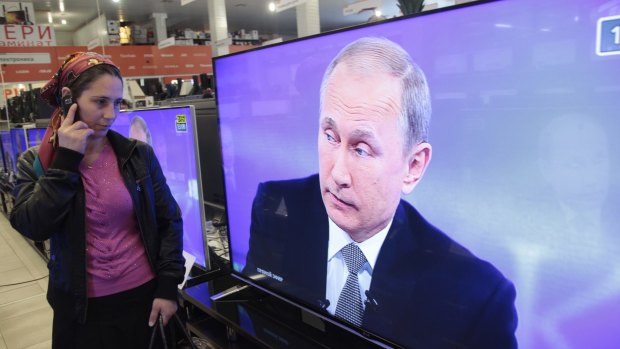 A Chechen woman speaks on the phone as she looks at a TV image of President Vladimir Putin speaking during his live televised call-in show on Thursday.