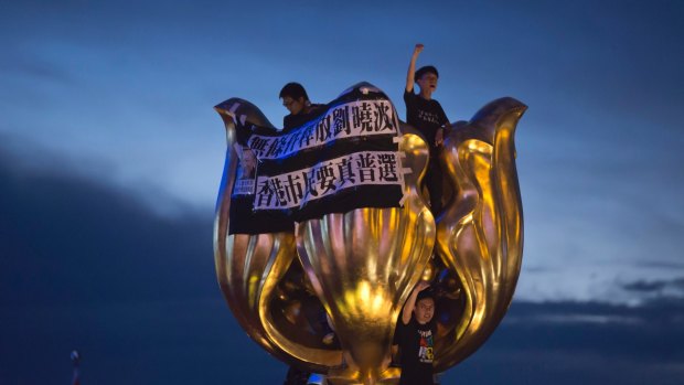 Pro-democracy activists shout slogans from the top of the golden bauhinia statue, which was given to Hong Kong by Beijing in 1997.