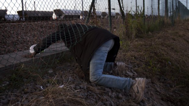 A migrant crawls under a fence in an attempt to access the Channel Tunnel in Calais in August.