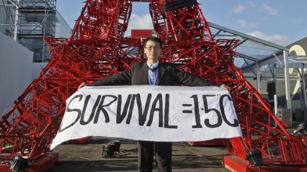 A representative of a NGO displays a banner supporting a target to keep global warming below 1.5 degrees in front of a reproduction of the Eiffel tower at the Paris climate summit.
