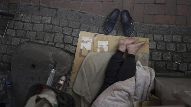 A homeless man rests under a pedestrian bridge.