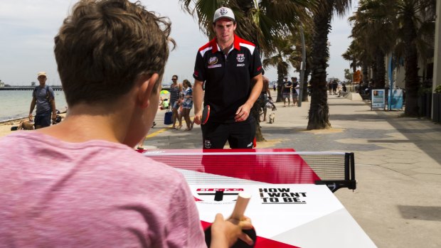 St Kilda footballer Paddy McCartin plays a game of pop-up table tennis against Saints fan Oliver Diano at St Kilda beach.
