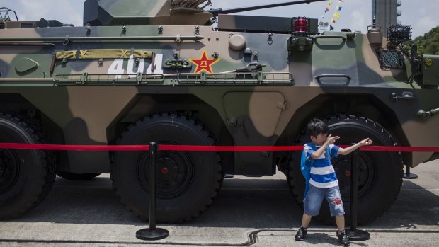 Aspirations of a nation: a child pretends to hold a gun while posing for a photograph in front of a People's Liberation Army tank.