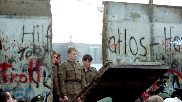 East German border guards watch  as part of the Berlin Wall is torn down.