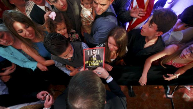 Marco Rubio, with back to camera, autographs a Time magazine with his image on the cover. 
