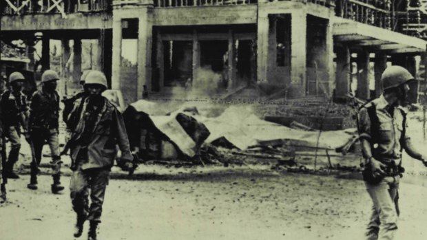 Indonesian police walk away from the smoking ruin after demonstrators had burnt the headquarters of the Communist Party, "PKI", to the ground in Djakarta in October 1965.