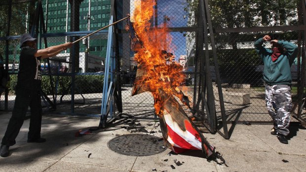 An American flag is set alight in front of the US Embassy in Mexico City on Friday.