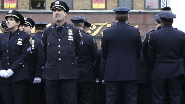 Law enforcement officers stand, with some turning their backs, as New York City Mayor Bill de Blasio speaks on a monitor outside the funeral for NYPD officer Wenjian Liu.