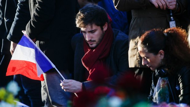 A mourner holds a French national flag as he pays his respects to victims of the terrorist attacks, at Place de la Republique.