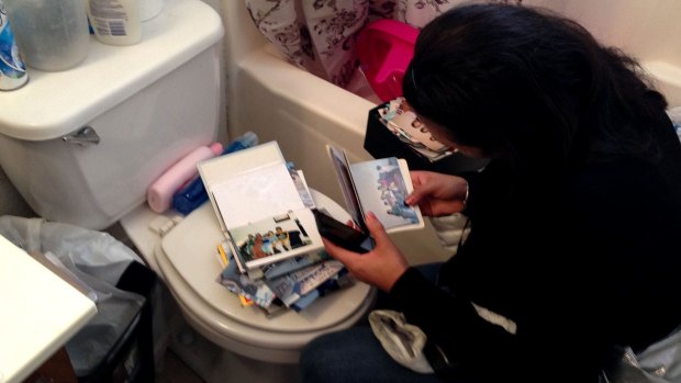 A woman straddles the toilet and rifles through photo albums.