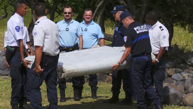 French gendarmes and police carry a piece of debris from MH370, which was found on the beach in Saint-Andre, on the French Indian Ocean island of Reunion.