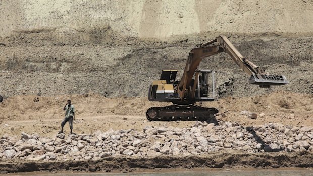 A labourer stands as a bulldozer works on a new section of the Suez canal during a media tour in Ismailia, Egypt.