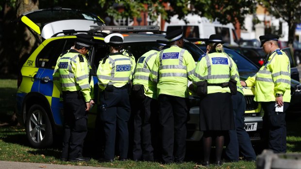 Police and community support officers gather round a police vehicle near where the incident happened.