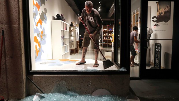 Scott McRoberts helps clean up broken glass after a violent crowd broke windows in University City, Missouri. 