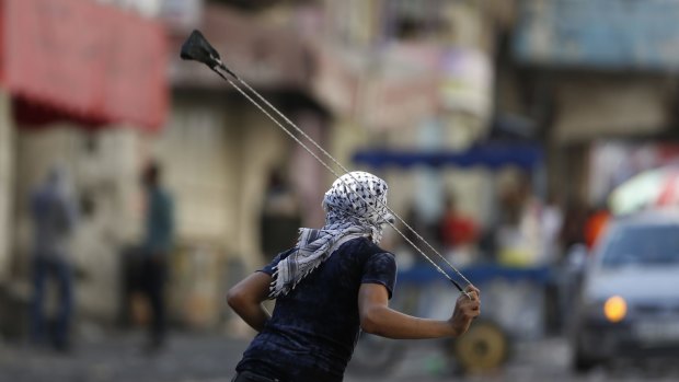 A Palestinian protester uses a sling shot during clashes with Israeli soldiers following a mass funeral in Hebron on Saturday. 