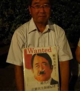 A protester with a sign showing Japanese PM Shinzo Abe as World War II Nazi dictator Adolf Hitler.