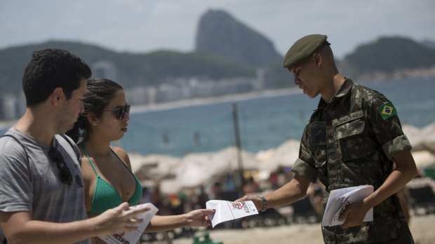A soldier distributes a pamphlet about the mosquito that spreads the Zika virus on the edge of the Copacabana beach in Rio de Janeiro, Brazil.