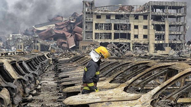 A firefighter walks among damaged vehicles as smoke rises amidst shipping containers at the site of Wednesday night's explosions.