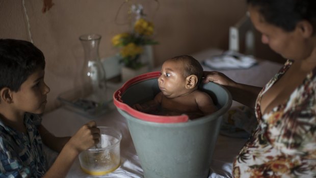 Elison, 10, watches as his mother Solange Ferreira bathes Jose Wesley in a bucket at their house.