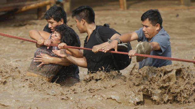 People hold onto a rope as they wade through flood waters to safety in Lima, Peru, at the start of this month's storms.