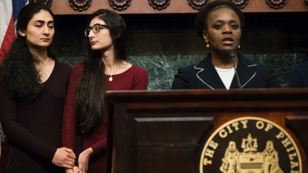 Farzaneh Ahmadi Darani, left, and her sister Shadi Ahmadi Darani hold each others' hands during a news conference in Philadelphia. Attorney Ayodele Gansallo speaks.