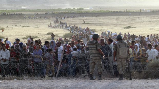 Turkish soldiers stand guard as Syrians wait behind the border fences near the southeastern town of Suruc in Sanliurfa province, on Thursday.