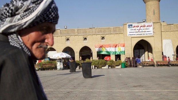 An elderly man sits in the centre of Irbil near a campaign poster urging people to vote yes.