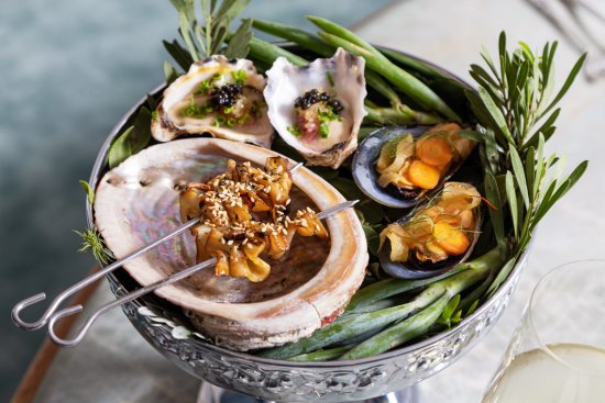 A mini seafood tower holding oysters with finger lime, barbecued abalone skewers and mussel escabeche.