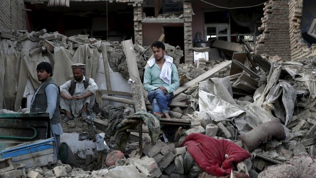 Men sit amid debris at the site of a truck bomb blast in Kabul last week.
