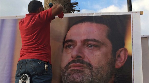 Workers hang a poster of outgoing Prime Minister Saad Hariri with Arabic words that read, "We are all Saad," on a seaside street in Beirut, Lebanon, on Thursday.