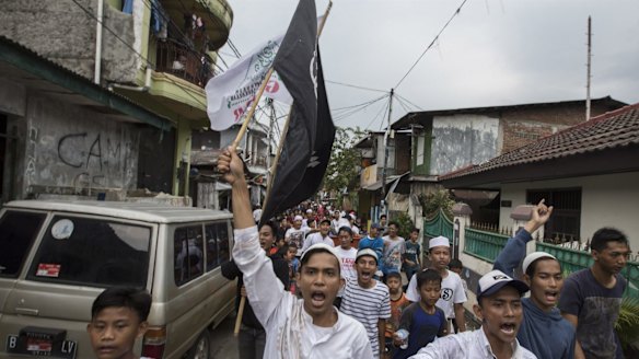 Indonesian youths march through their neighbourhood with an Islamic flag after quick count results showed Anies Baswedan heading for victory.