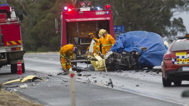 Emergency services examine the wreckage of a car that hit a truck in a head-on collision.