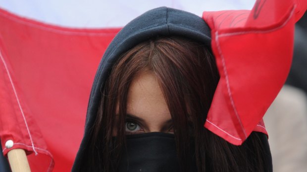 A masked protester holds a Polish flag during a right-wing nationalist march in Warsaw, demonstrating against EU-proposed quotas to spread the human tide of refugees around Europe.