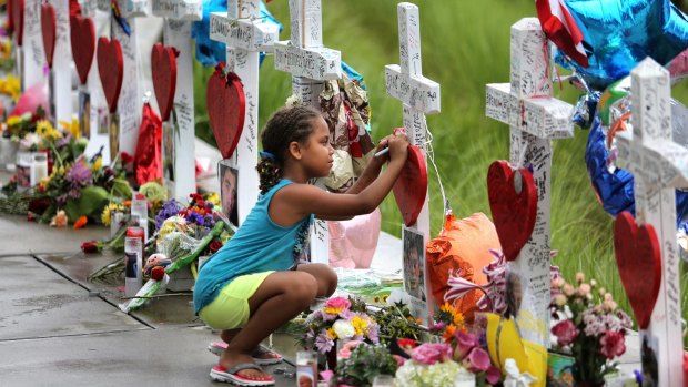 Seven-year-old Mekiha Thomas of Orlando signs one of the 49 crosses at a makeshift memorial outside Orlando Regional Medical Centre. The crosses were erected by an Illinois man to honour each of the victims in the Pulse nightclub shooting.