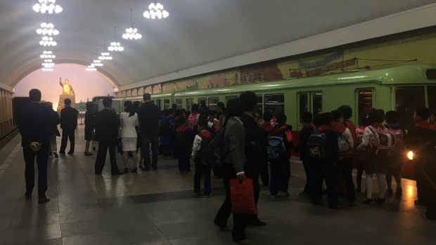 School children in the underground, as a gold statue of Kim Il-sung towers over commuters.